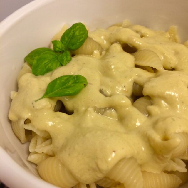 noodles and cheese in bowl with shell noodles and fresh basil leaves