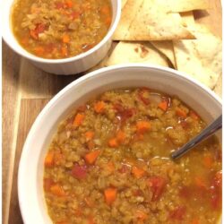 lentil soup in 2 white bowls on wood cutting board with homemade tortilla chips