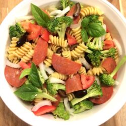 pizza pasta salad in white bowl on wooden cutting board