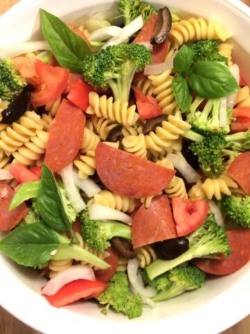 pizza pasta salad in white bowl on wooden cutting board