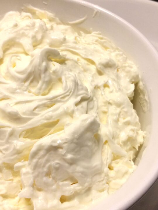 Close up view of homemade mascarpone in a white bowl.