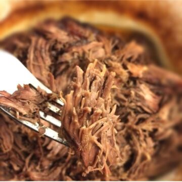 Finished shredded beef close up with fork bringing a portion to the foreground.