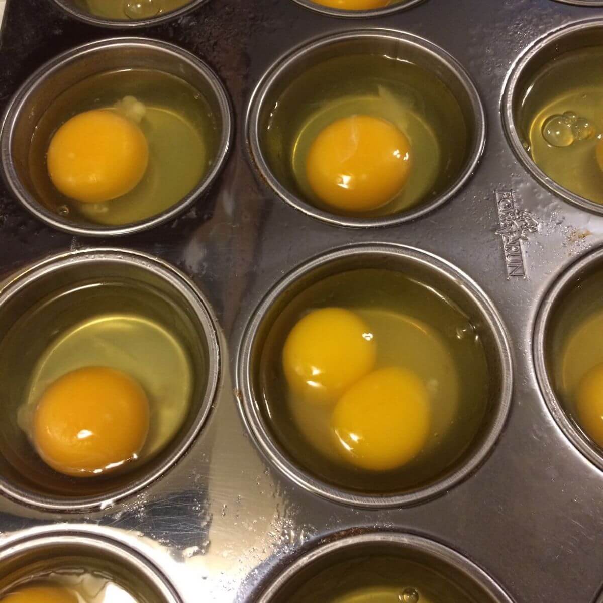 raw eggs dropped into muffin tin, 1 with a double yolk