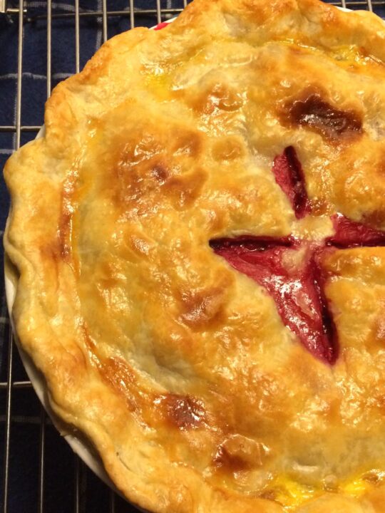 baked raspberry rhubarb pie close up on wire rack.