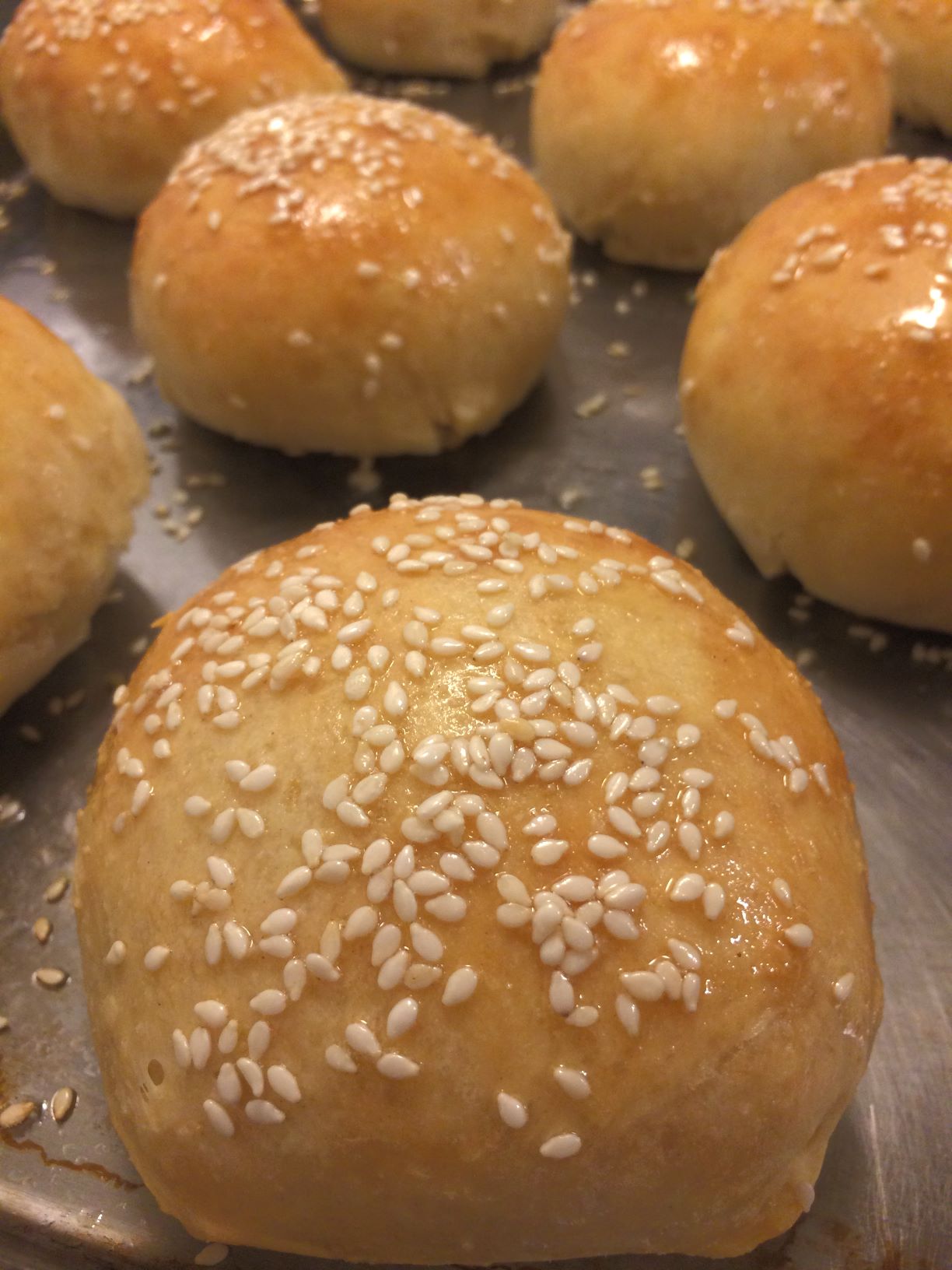 burger buns with sesame seeds on top on baking sheet