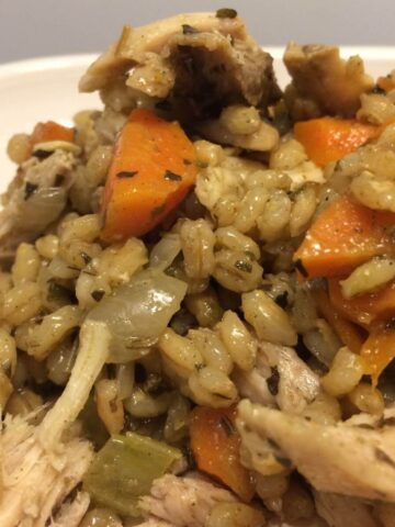 chicken and barley with carrots and onions on white plate