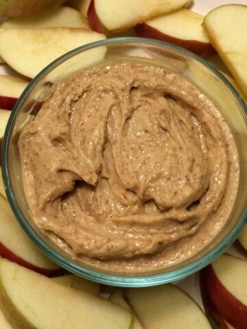 almond butter greek yogurt dip in glass bowl with apple slices surrounding it
