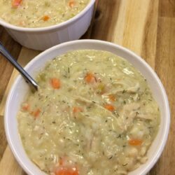 avgolemono with chicken and rice in white bowls with silver spoon on a wooden cutting board