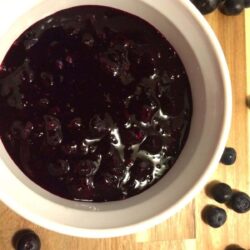 blueberry pie filling in white bowl with blueberries sprinkled on the side