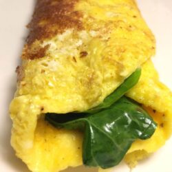 cheesy greens omelet close up with chard stcking out the end on white plate