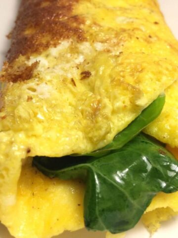 cheesy greens omelet close up with chard stcking out the end on white plate