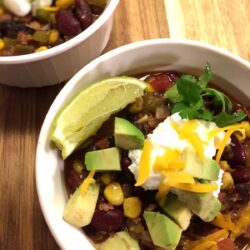 bowl of chili topped with dollop of Greek yogurt, shredded cheddar cheese, avocado chunks, and slice of lime