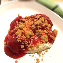 deconstructed strawberry cheesecake layered on a white plate with a green towel with black stripe blurred in the background