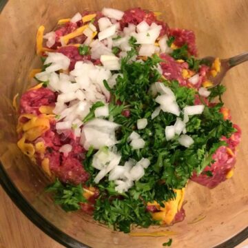 Ingredients for hamburger patties in a glass bowl with fork