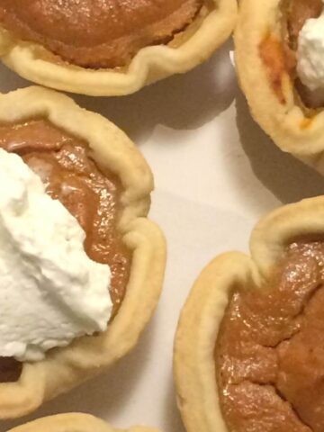 mini pumpkin pies, 2 with whipped cream on top on white plate
