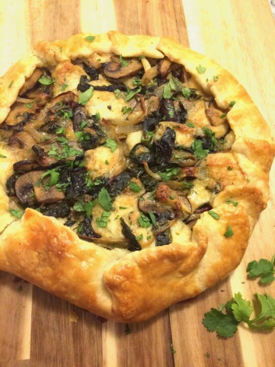 mushroom and chard galette on wooden cutting board with fresh cilantro on top and on board