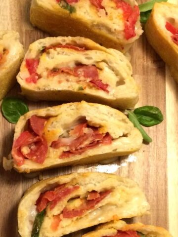 pepperoni pizza bread in slices with fresh basil on wood cutting board