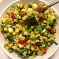 corn salad in white bowl with metal spoon in upper right corner of bowl