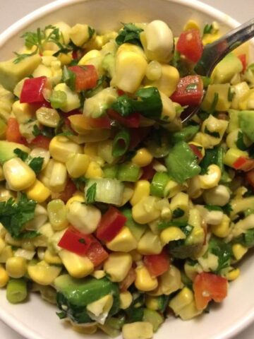 corn salad in white bowl with metal spoon in upper right corner of bowl