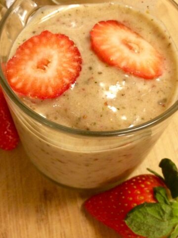 strawberry banana orange kale smoothie in glass mug with fresh strawberries on the side