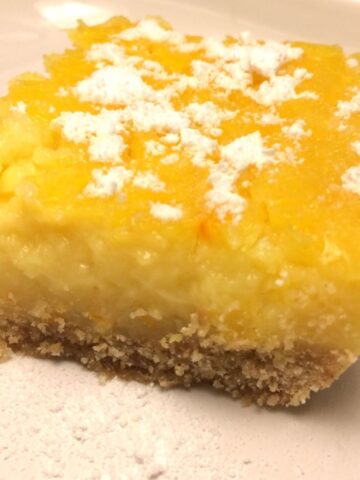 lemon bar on white plate with powdered sugar on top