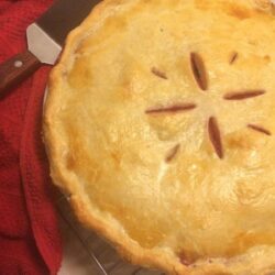 triple berry pie with design in lid, red towel to the left with pie cutter on towel