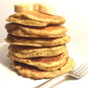 banana oat pancakes stacked with banana slices on top on white plate with fork on plate in front