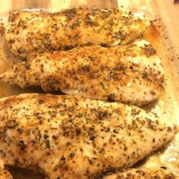 baked chicken lined up in a glass cake pan on top of a wooden board