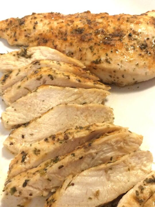 baked chicken with 1 breast sliced and lined up and 1 breast in the background all on a white plate