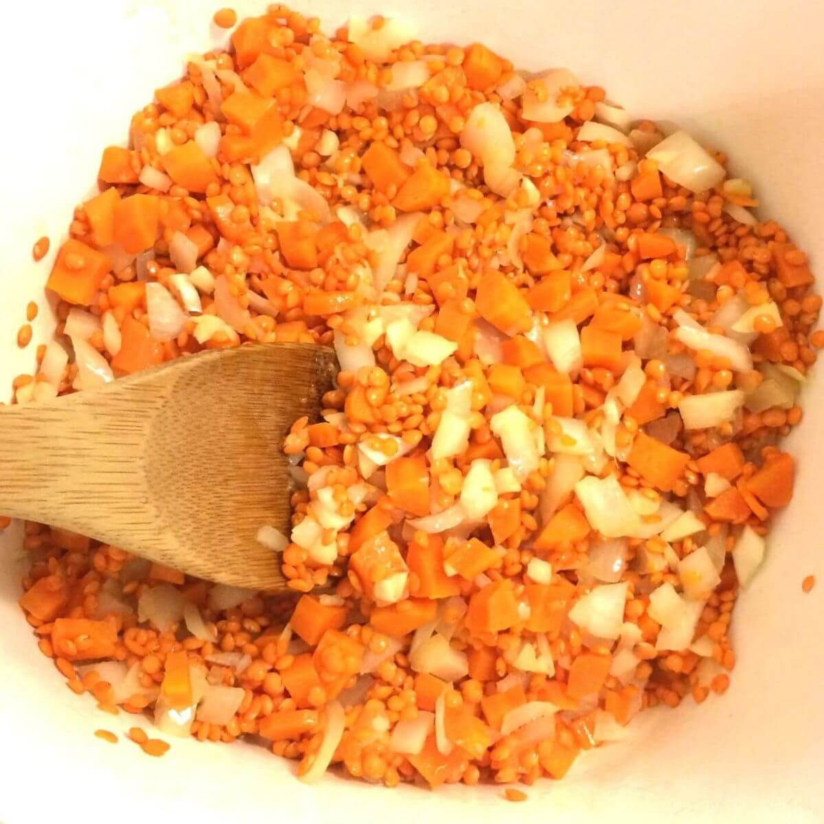 lentil soup veggies sautéing in Corning Ware with wooden spoon