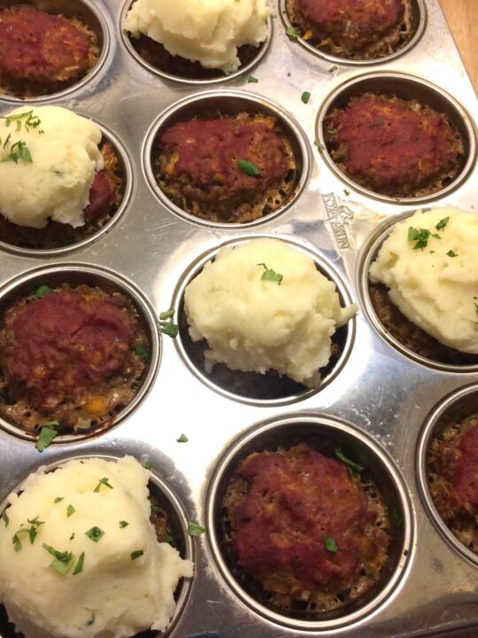 meatloaf muffins in muffin tin with mashed potatoes topped on a few and garnish of fresh parsley