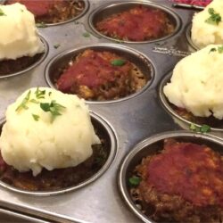 meatloaf muffins in muffin tin with a few topped with mashed potatoes and garnished with fresh parsley