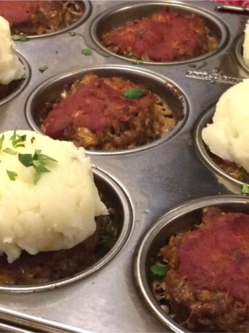 meatloaf muffins in muffin tin with a few topped with mashed potatoes and garnished with fresh parsley