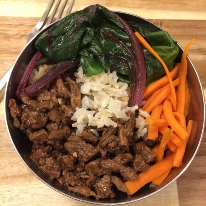 mongolian beef bowl with ingredients separated in a stainless steel bowl with a fork on the side all on a wooden cutting board