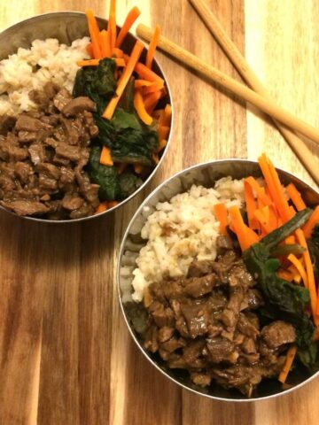 Two mongolian beef bowls with ingredients separated in stainless steel bowls with chopsticks on the side all on a wooden cutting board