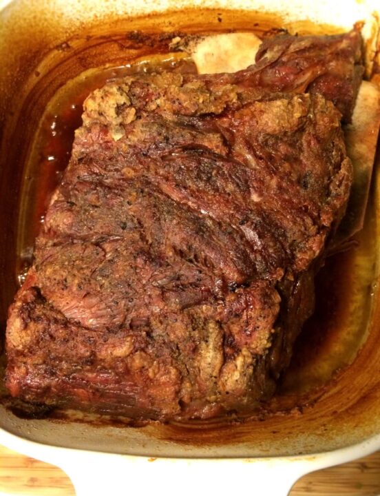 Bone in pork shoulder roast with crackling in juices in a large Corning Ware Dutch Oven.