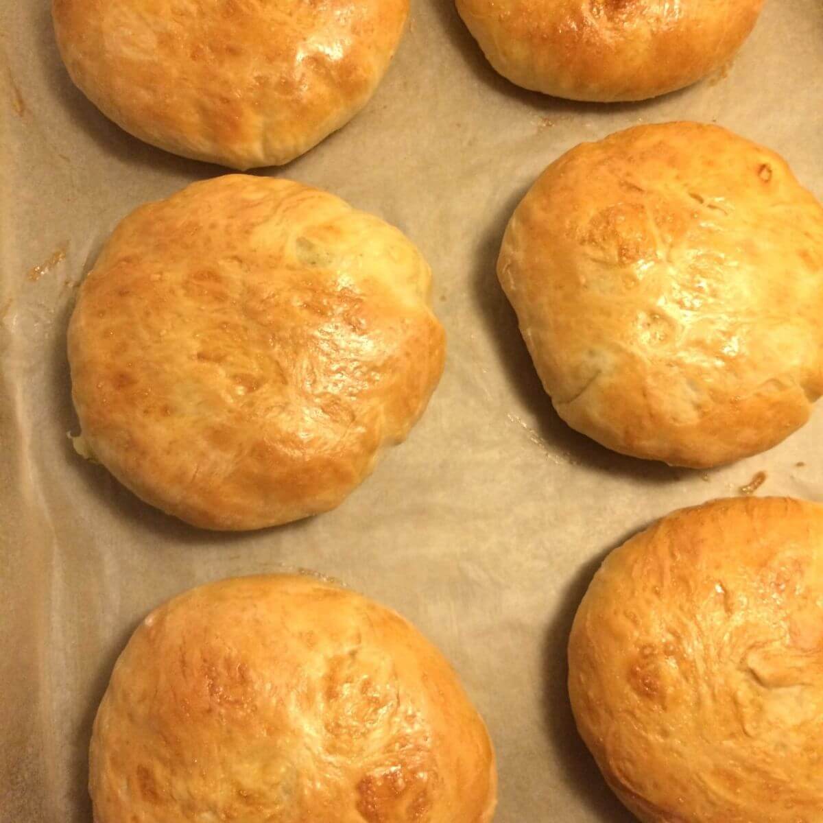 baked potato bread loaves golden brown lined up in two rows on parchment paper.