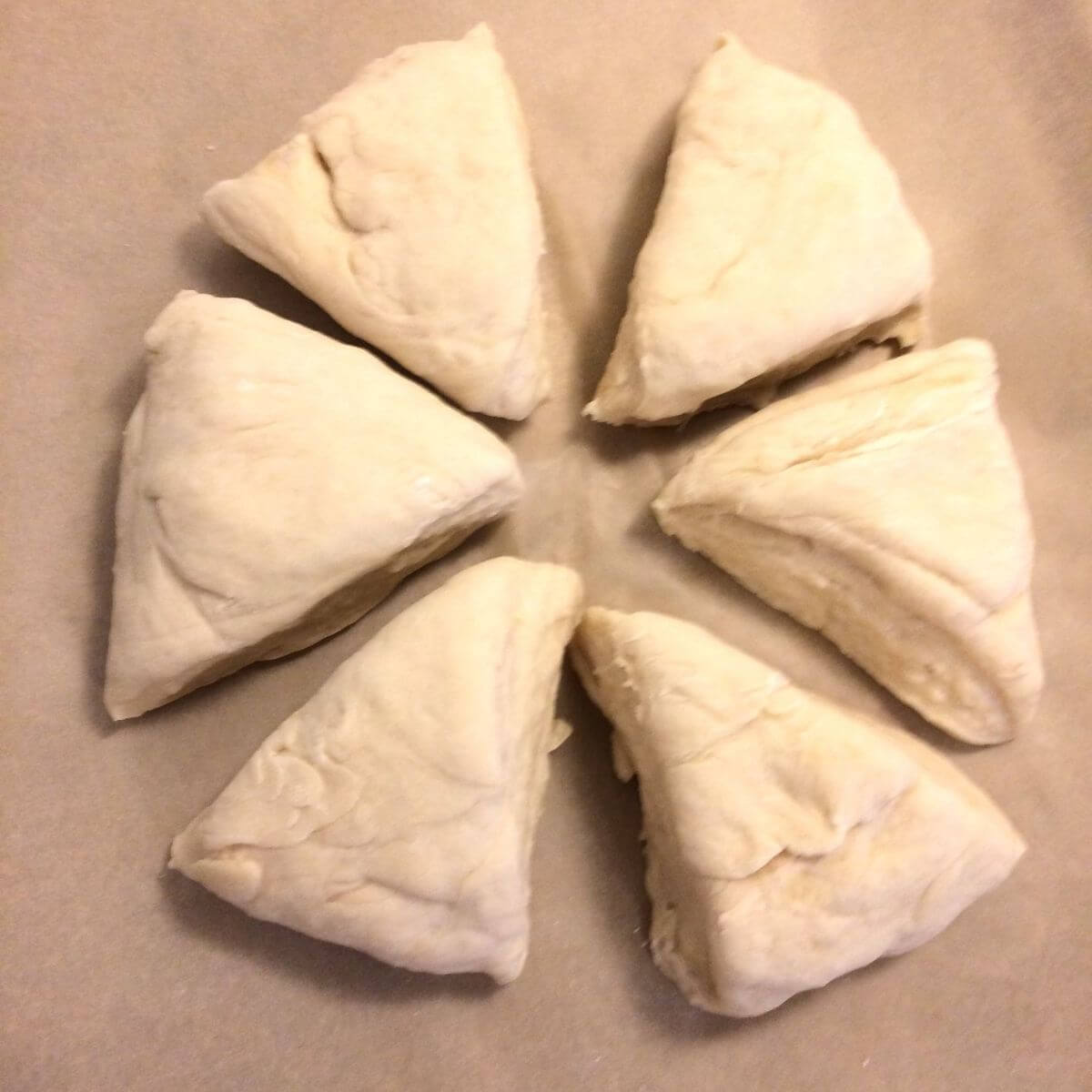 Risen dough cut into 6 equal portions triangle shaped, resting on parchment paper.