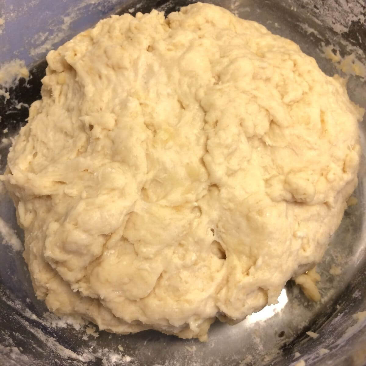 Raw dough combined into a ball, still pretty sticky and placed in glass bowl.
