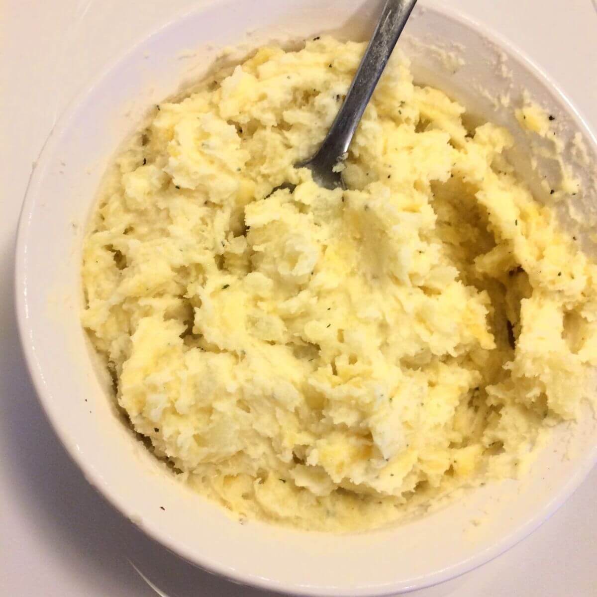 Mashed potato filling mixed with cheese, Greek yogurt, and spices in white bowl with white background and silver spoon in bowl.