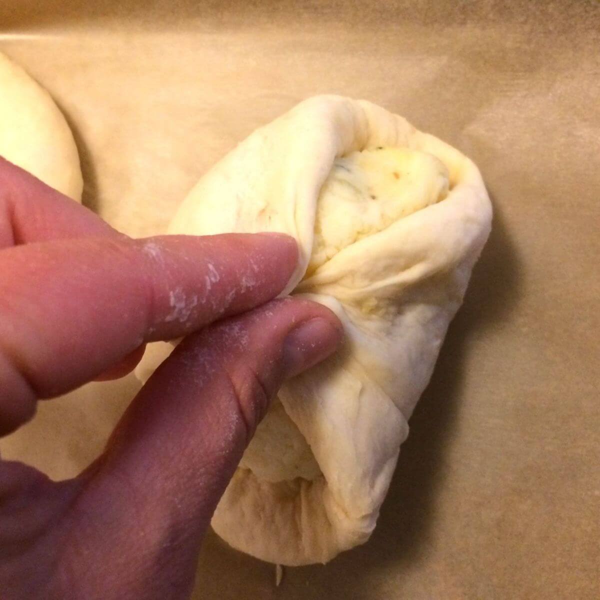 1 dough portion being punched closed around the filling with fingers in image.