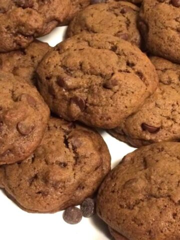 double chocolate chip cookies piled on a white plate with chocolate chips loosely scattered