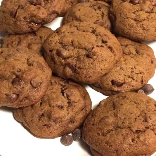 double chocolate chip cookies piled on a white plate with chocolate chips loosely scattered