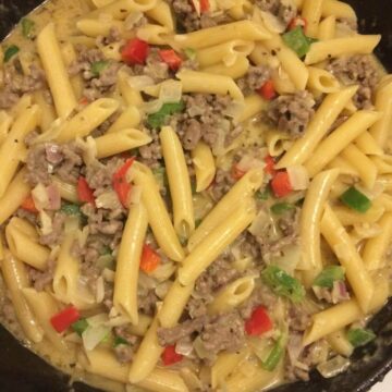 creamy beef rotini in cast iron skillet with penne noodles and multi-colored bell peppers