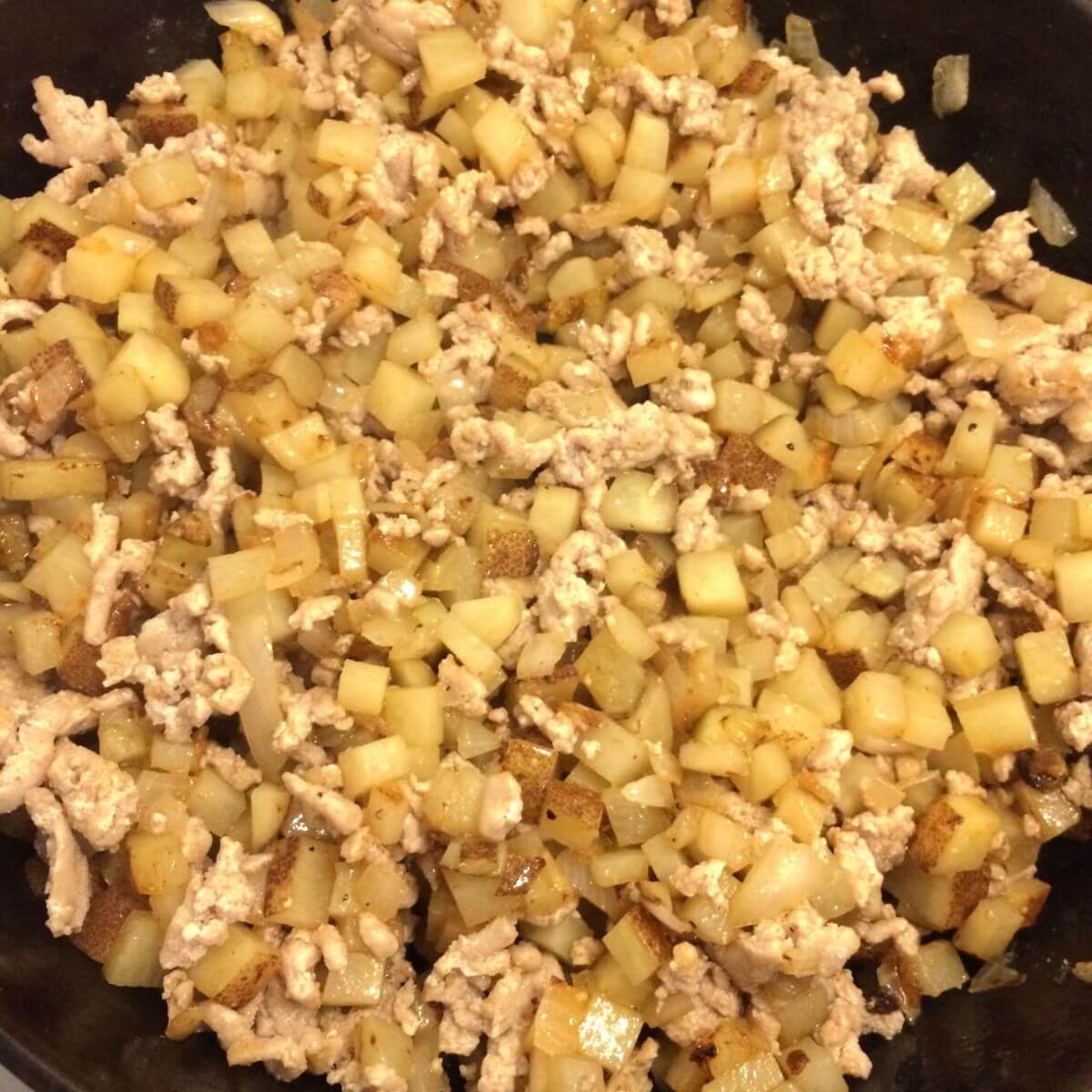 diced potatoes, onions, and cooked ground pork in a cast iron skillet
