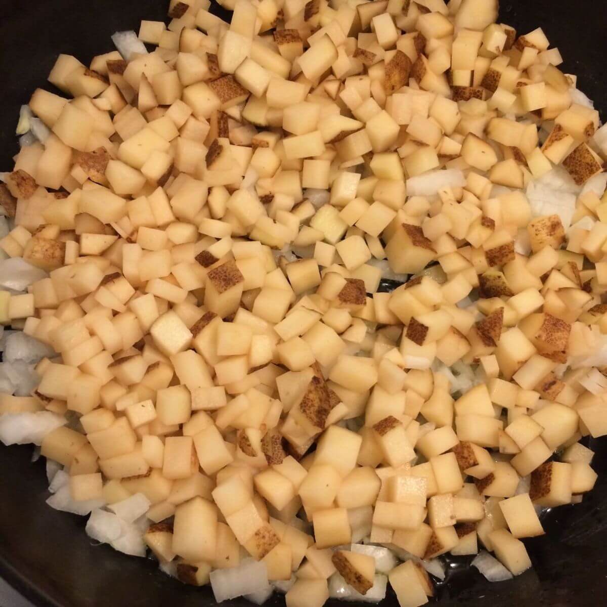 diced potatoes and diced onions cooking in a cast iron skillet