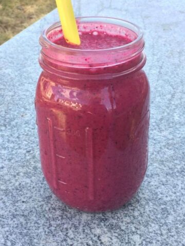 red beet smoothie with yellow straw on granite with grass in the background