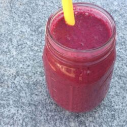 red beet smoothie in mason jar with yellow silicone straw on granite