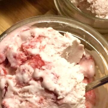 finished frozen strawberry ice cream scooped into glass jar close up view with spoon handle sticking out of ice cream.