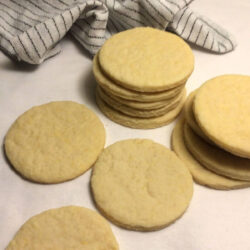 baked cut out sugar cookies with 2 stacks and 3 single cookies in the front with a white towel with black strips in the back
